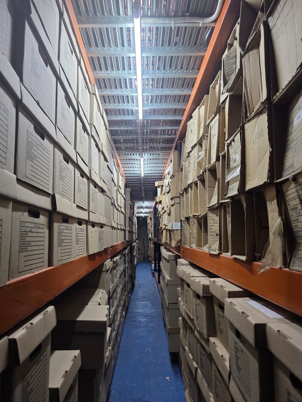 Pasillo angosto del depósito de SOS Archivos con cajas de archivo a ambos lados